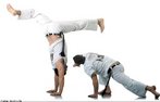 O jogador  direita ataca com uma Cabeada e o outro se defende com uma bananeira com as pernas separadas. <br> Por Fernando Fischer - Imagens MPIB <br> <br> Palavras-chave: capoeira, fundamentos, movimentos,combate.