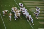 Imagem das equipes alinhadas em lados opostos de uma linha de scrimmage. <br><br> Palavras-chave: esporte, futebol americano, linha de scrimmage.